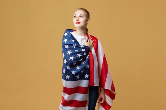 attractive blonde proudly poses with an American flag. photo shoot in the studio on a yellow background