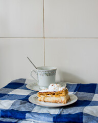 Pastel de hojaldre dulce relleno de crema, acompañado de una taza de café sobre un mantel a...