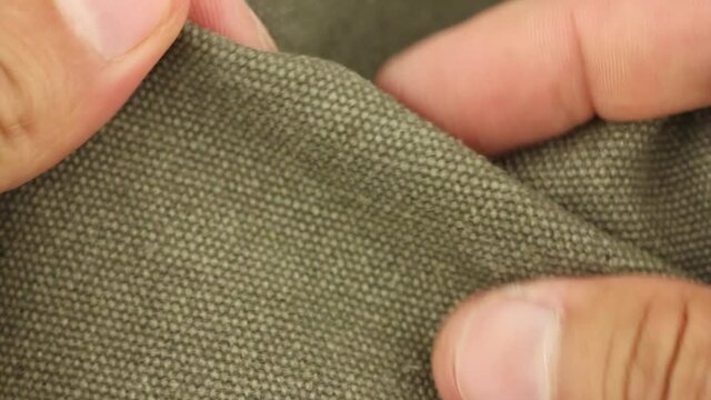human hand tests, rumples and crumples green tarpaulin fabric textile material, close-up view
