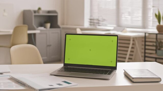 Tilting left of laptop computer with chroma key on screen on desk in office at daytime