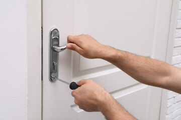 Handyman with screwdriver repairing door lock indoors, closeup - obrazy, fototapety, plakaty