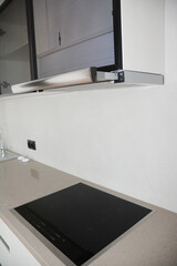 A close-up of a modern kitchen design with a stone countertop, a black electric induction cooktop, and an integrated telescopic kitchen extractor, cooker hood.