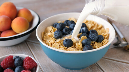 Cornflakes with milk and blueberries in bowl on a wooden table, closeup view. Breakfast food