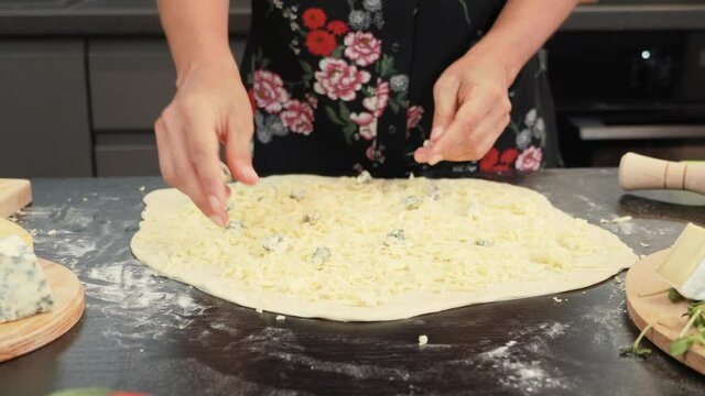 Hands putting blue dorblu cheese on pizza base. Female chef making pizza in restaurant kitchen
