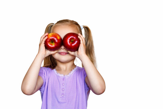 Little Girl On A White Background Holds Apples In His Hands. The Child Holds Two Red Apples In Front Of Her Eyes