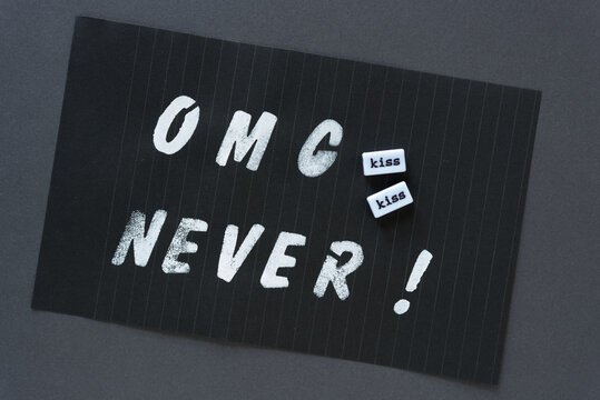the words "OMG never!" in alpha/numeric plastic stencil letter type - hand painted in white acrylic paint - on black pad paper with faint lines and word beads with "kiss, kiss" - on dark gray paper