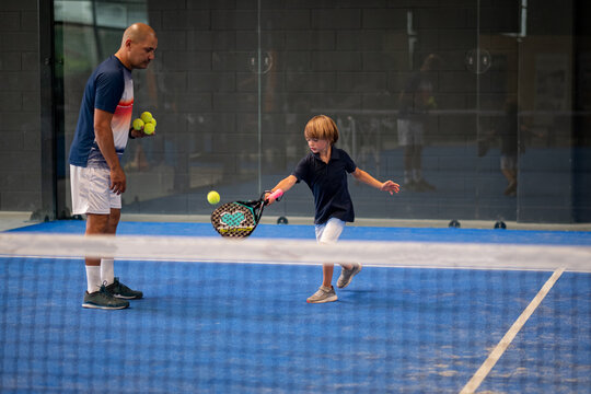 Monitor teaching padel class to child, his student - Trainer teaches little boy how to play padel on indoor tennis court
