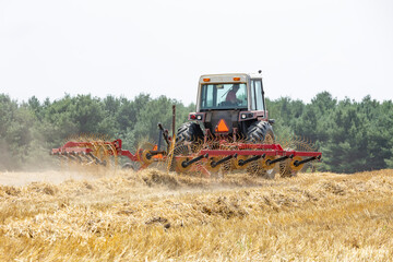 Fototapeta premium A tractor and rake raking wheat straw in a farm field.
