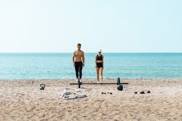 Sportive young couple, man and woman start training on the beach with sports inverter, preparation...