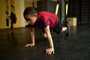 Latino american schoolboy perform exercise using gym equipment, train legs on special belts. Set...