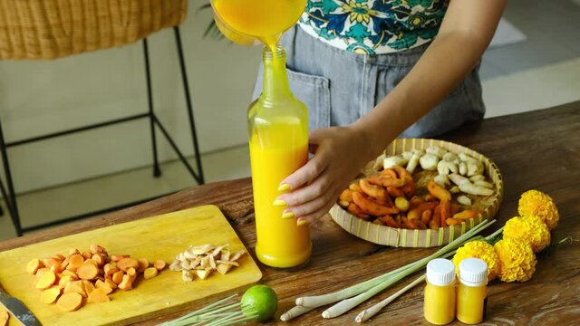 Close up of woman preparing homemade Jamu drink- Indonesian herbal beverage with natural ingredients: turmeric, ginger, lime, lemongrass, tamarind, lemongrass in kitchen. Healthy lifestyle