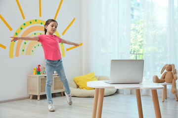 Cute little girl taking online dance class at home