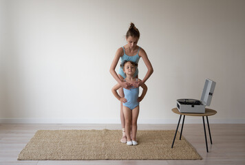 an adult ballerina girl shows the movements to a little girl a child who stands and obediently...