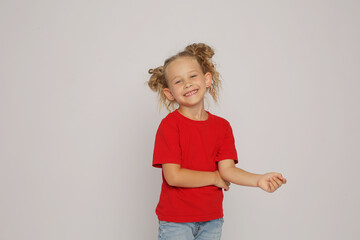 a beautiful blonde girl with ponytails in a red T-shirt and jeans shows emotions happiness
