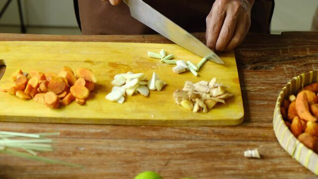 Close up of woman cutting herbs, roots and spices for homemade Jamu drink- Indonesian herbal beverage with natural ingredients: turmeric, ginger, lime, lemongrass, tamarind, lemon in kitchen.