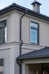 close-up view of house with gray fold roof and plums and filing of roof overhangs with soffits and brick stone pipe covered with metal sheets and black smoke box