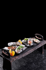Assorted fresh open oysters in a plate with ice and lemon on a black texture background, top view. High quality photo
