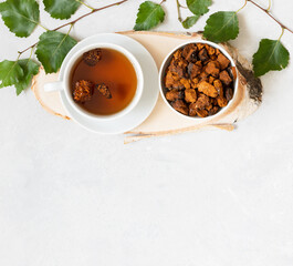 Chaga drink. Chaga tea, chopped pieces of mushroom chaga and birch leaves on a white background. Organic healthy drink with birch mushroom. Copy space, top view, flat lay.