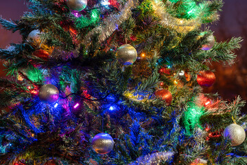 Fototapeta premium Green spruce branches with red and silver balls, toys and lights hanging. Christmas tree decorations background. New year concept