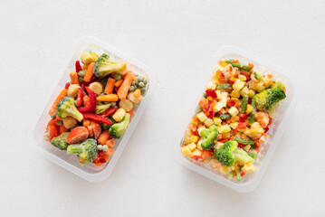 Frozen vegetable salad in containers on a white concrete background. Vegetable mix for cooking. View from above.