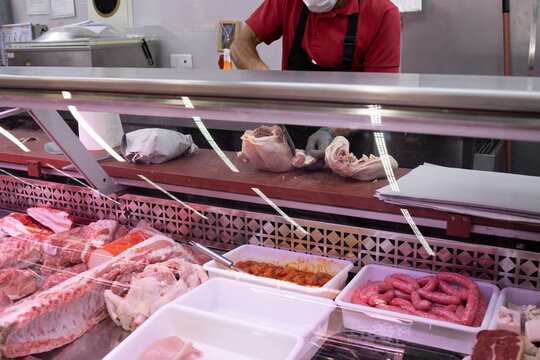 A butcher behind the counter cutting a chicken.
