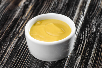 yellow mustard sauce in a sauce bowl on a dark wooden background. High quality photo