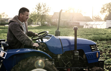 Farmer driving a tractor across the field. Agro industry, agribusiness. Farming, agriculture. Countryside farmland. Small farms. Work in the agricultural industry.