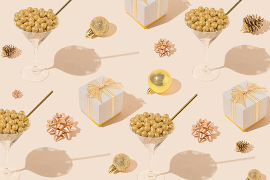 Creative pattern made with martini glasses and straw, present boxes, golden bows and baubles on pastel beige background. Christmas or birthday party concept. Minimal style.