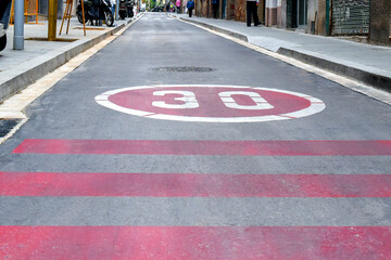 Symbol do not drive more than thirty kilometers per hour on road. Speed limit 30 and red lines of the crosswalk on the asphalt.