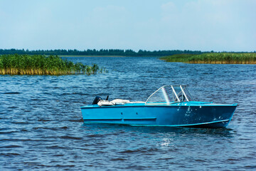 Aluminum blue fishing boat with a motor near the lake shore, fishing, active recreation, Background...