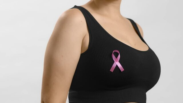 Young lady in a black top turning around to show ribbon sign on her chest to support pink October and females combating breast cancer. Anonymous slow motion studio shot video on white background.
