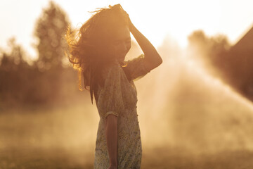 Tender lady in fashionable green dress playing her long wavy hair and posing in sun on outdoor. Joyful girl in modern clothes smiling..