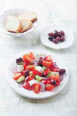 Simple salad with cherry tomatoes, feta cheese, kalamata olives, red pepper and fresh herbs. Bright wooden background.