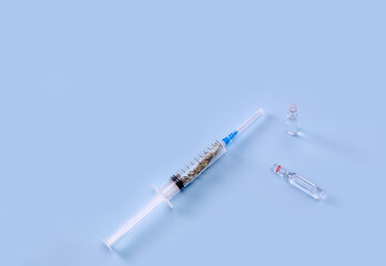 a sprig of wormwood (Artemisia) inside a syringe and an ampoule with medicine on a blue background. the concept of a cure for nature