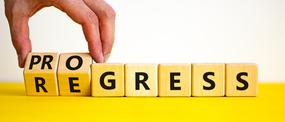 Regress or progress symbol. Businessman turns wooden cubes and changes the word 'regress' to 'progress'. Beautiful yellow table, white background, copy space. Business, regress or progress concept.