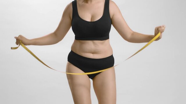 Chubby female in black bra and briefs happy dance with measure tape in her hands moving her hips. Studio still shot no face video.