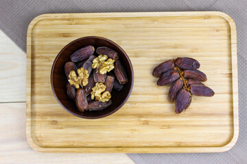 Obraz na płótnie Canvas Twig with dates on a wooden tray. Wooden bowl with dates and walnut kernels. Fruit on a wooden tray. Fruit dates. Walnut kernels.