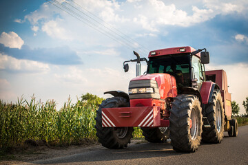 A farmer driving a big tractor to a corn field.