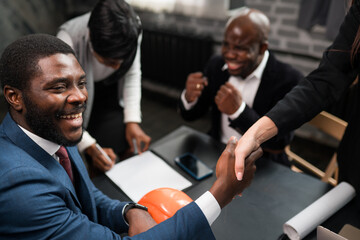 Happy african american businessman shaking hands with woman while negotiating with colleagues
