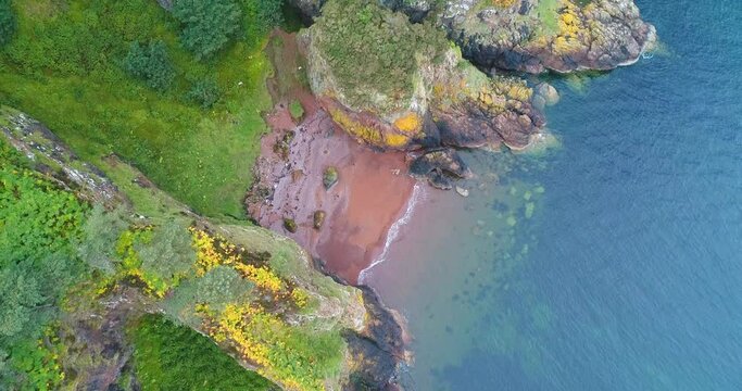4K top down landscape of Scottish coastline rock formation in the sea, beach between rocks with blue turquoise water moving forward along coastline
