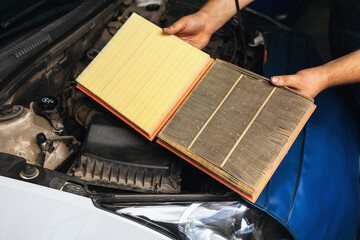 An auto mechanic shows for comparison two engine air filters, one old and the other new