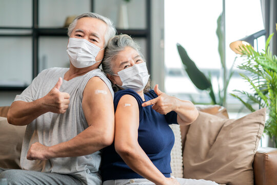 old asian senior couple wearing face mask virus protection happiness cheerful show bandage injection covid-19 vaccinated with hand gesture point and confident for virus protection 