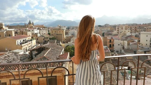 Beautiful woman looks out at cityscape of Palermo from balcony, Sicily, Italy