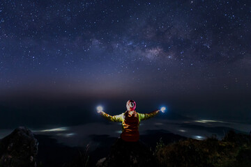 Fototapeta na wymiar Hiker woman standing with hands up and Colorful night sky with stars. Background with galaxy.