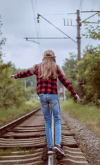 Baby girl on the railway tracks. Girl on the railroad in jeans, cap and shirt in a cell. Rear view.