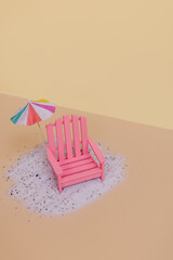 A pink beach foldable deck chair standing on sand surface next to a cocktail umbrella against beige...