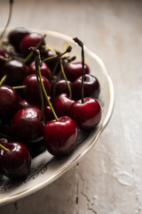 Juicy red cherries on a white plate on a light wooden background.