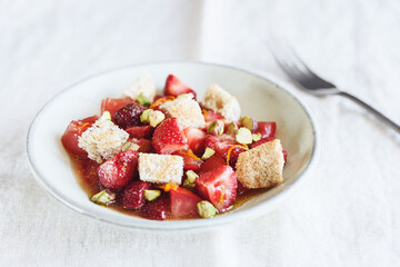 Delicious summer salad. Salad bowl with strawberries, tomatoes, pistachios and croutons in honey orange oil sauce on beige linen tablecloth