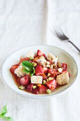 Delicious summer salad. Salad bowl with strawberries, tomatoes, pistachios and croutons in honey orange oil sauce on beige linen tablecloth