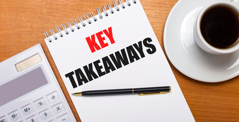 On a wooden table there is a white calculator, a white cup of coffee, a pen and a white notebook with the text KEY TAKEAWAYS. Business concept